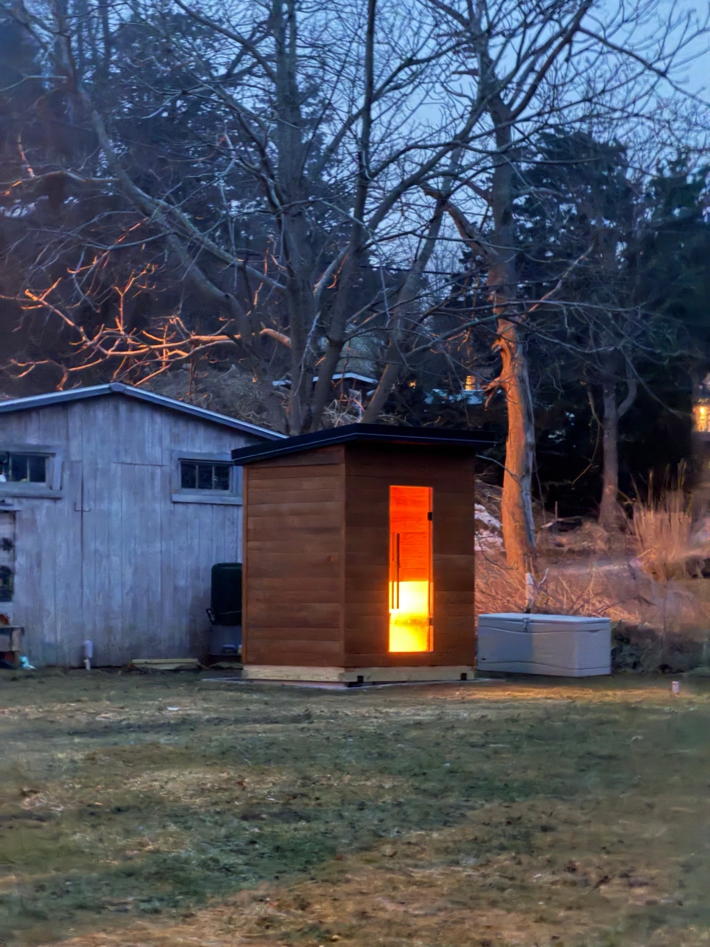 A Verdure outdoor sauna at dusk, its glass door lit from inside