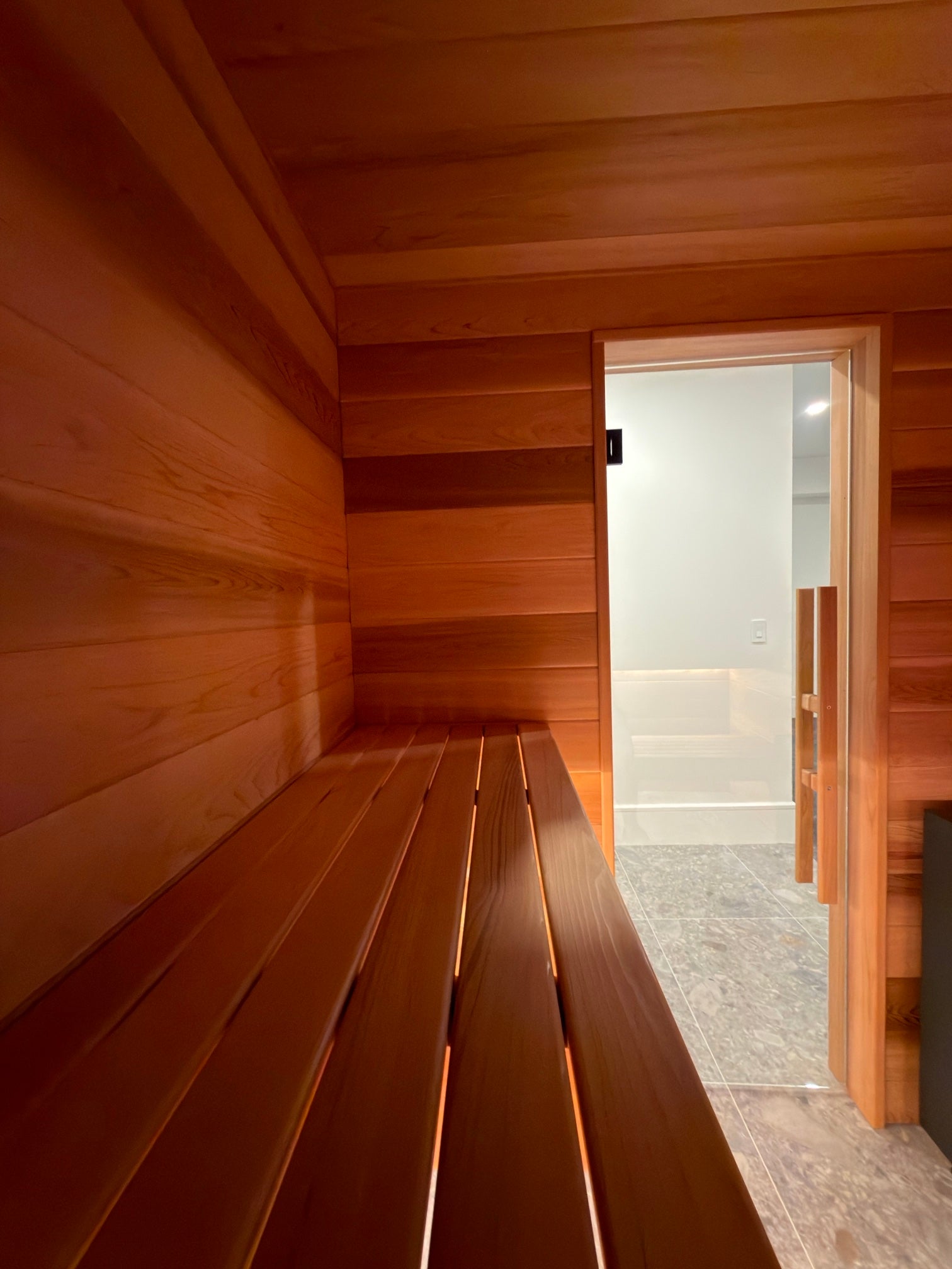 A cedar bench running toward the glass door of a built-in sauna